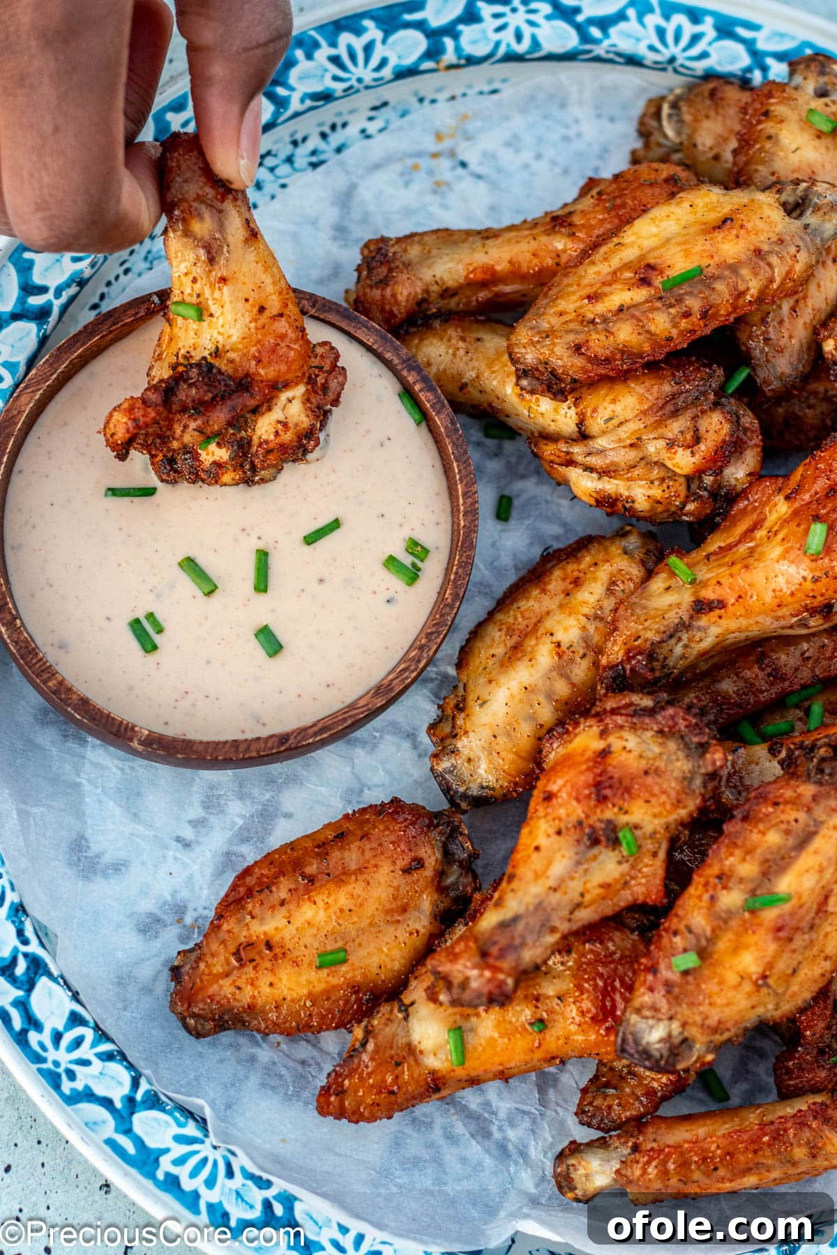 A baked chicken wing being dipped into a bowl of creamy ranch dressing.