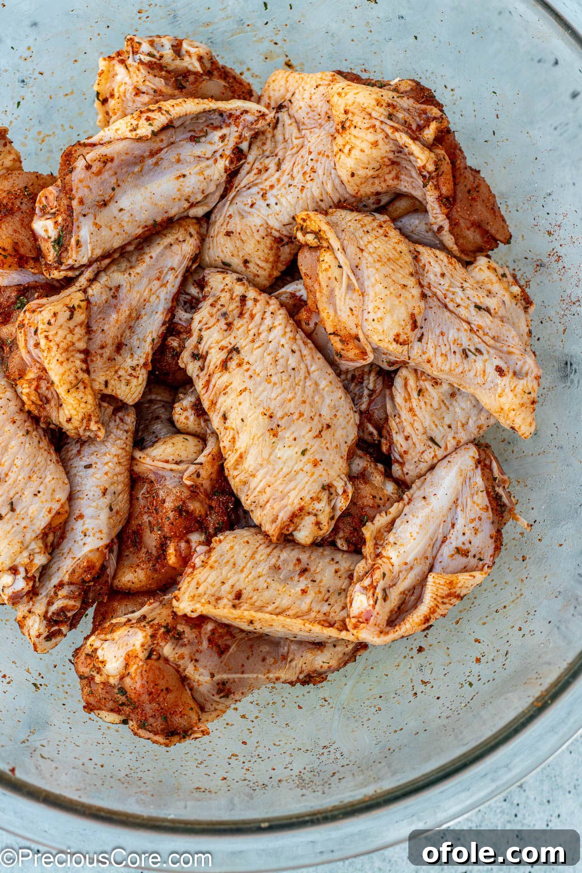 Raw chicken wings coated in a vibrant dry rub seasoning in a large mixing bowl.