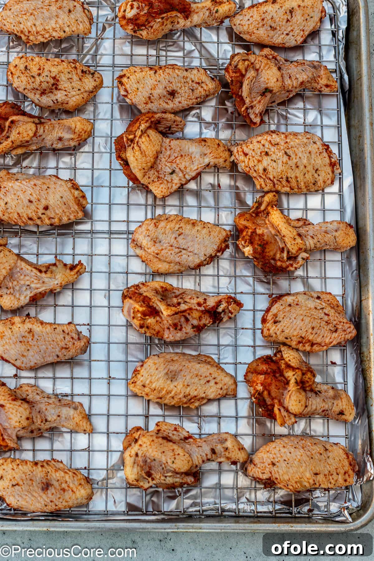 Seasoned chicken wings arranged in a single layer on an oven-safe wire rack over a foil-lined baking sheet.