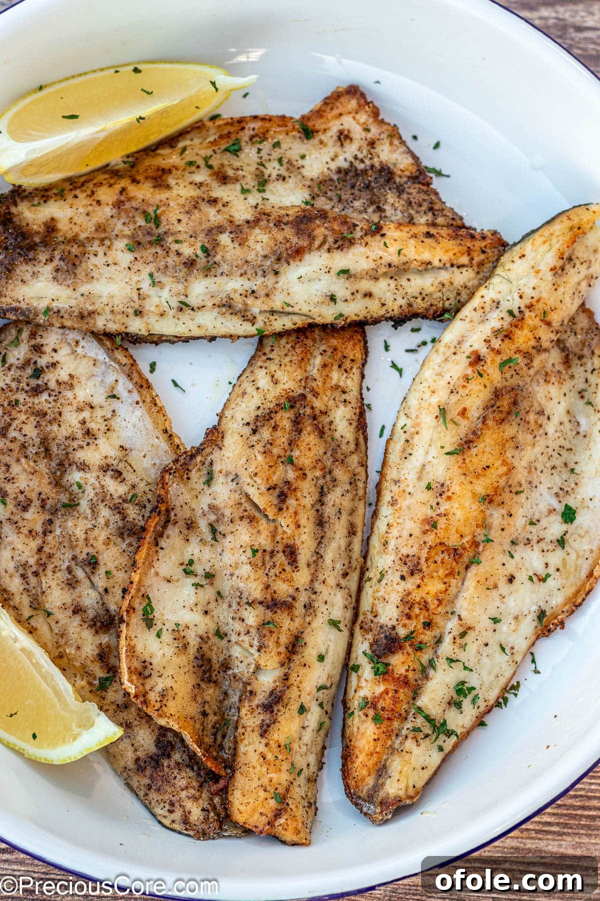 Pan Seared Sea Bass fillets on a white plate, garnished with fresh herbs.