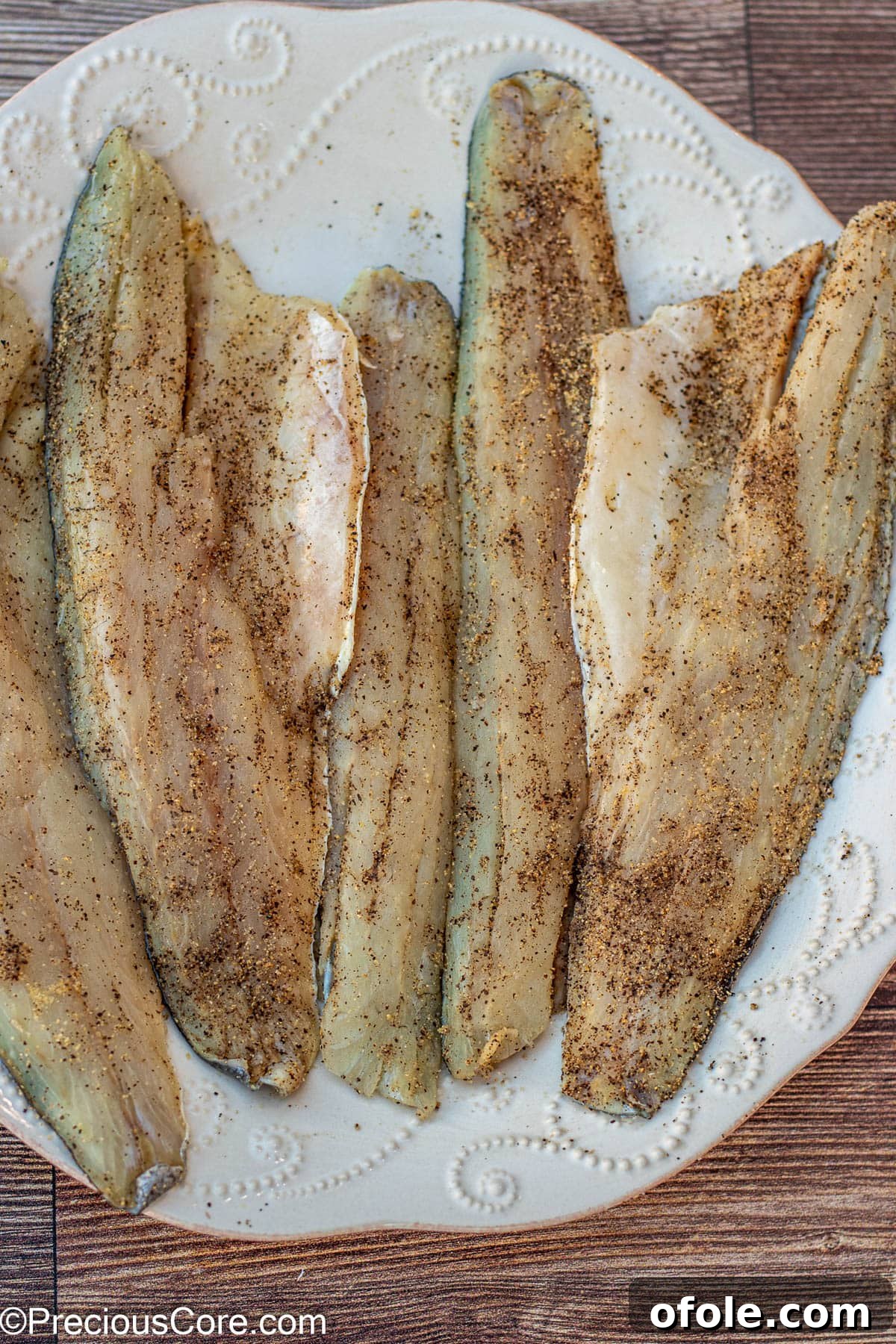 Seasoned sea bass fillets ready for cooking on a large plate.