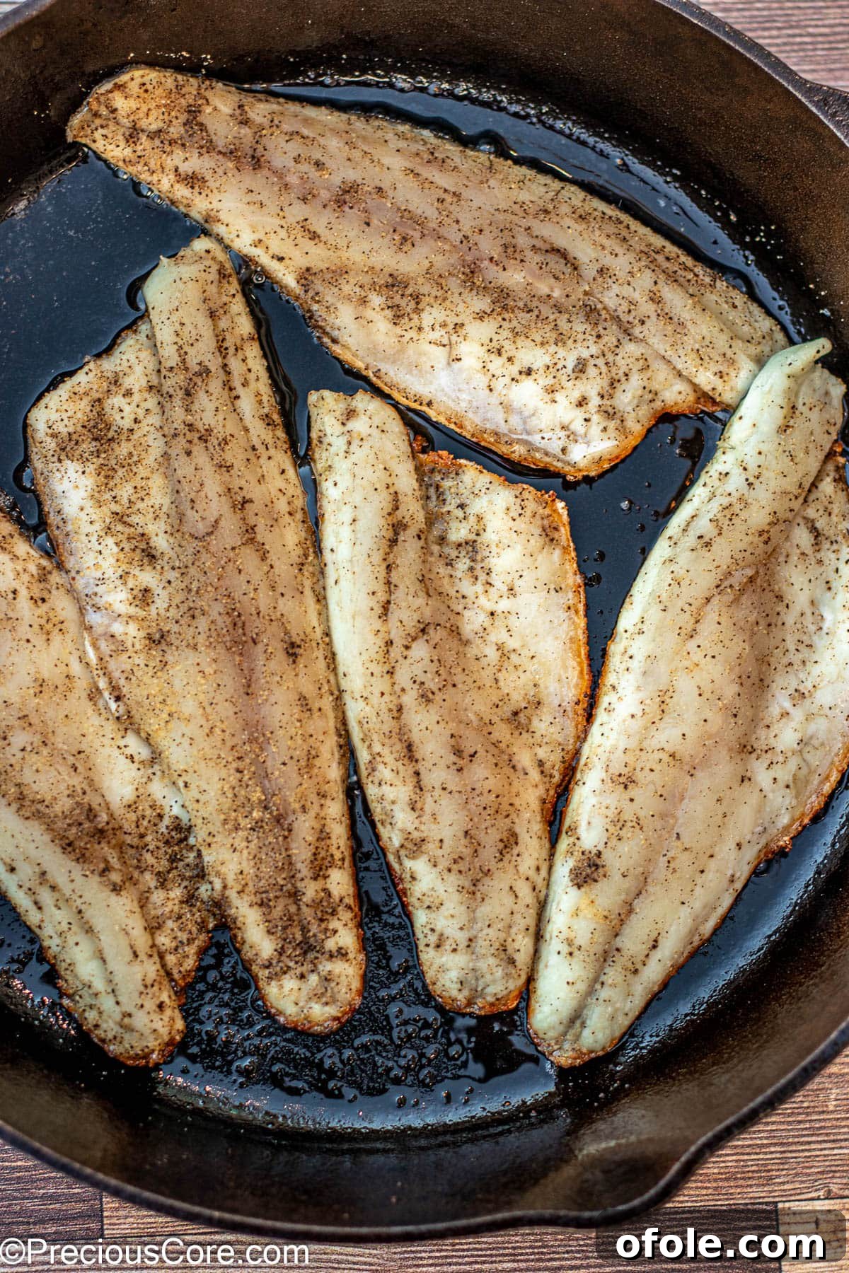 Fish fillets searing in a 12-inch cast iron skillet.