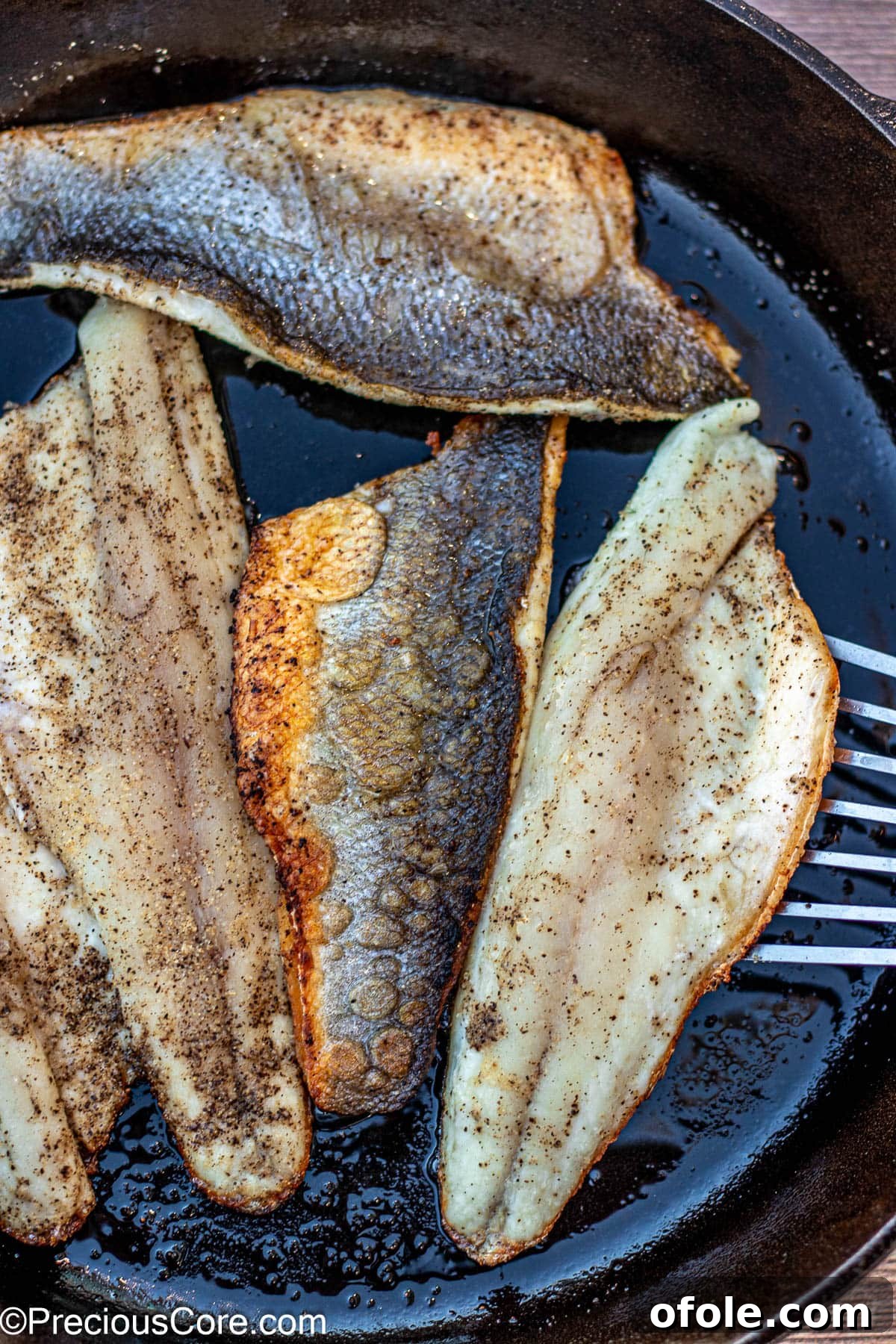 Fish spatula flipping perfectly cooked sea bass in a pan.