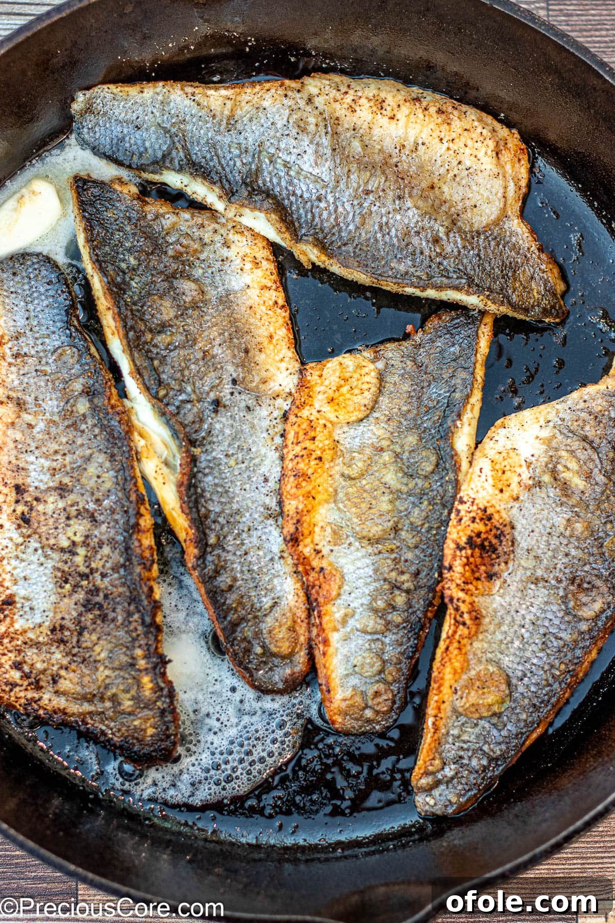 Butter melting and basting sea bass fillets in a cast iron skillet.