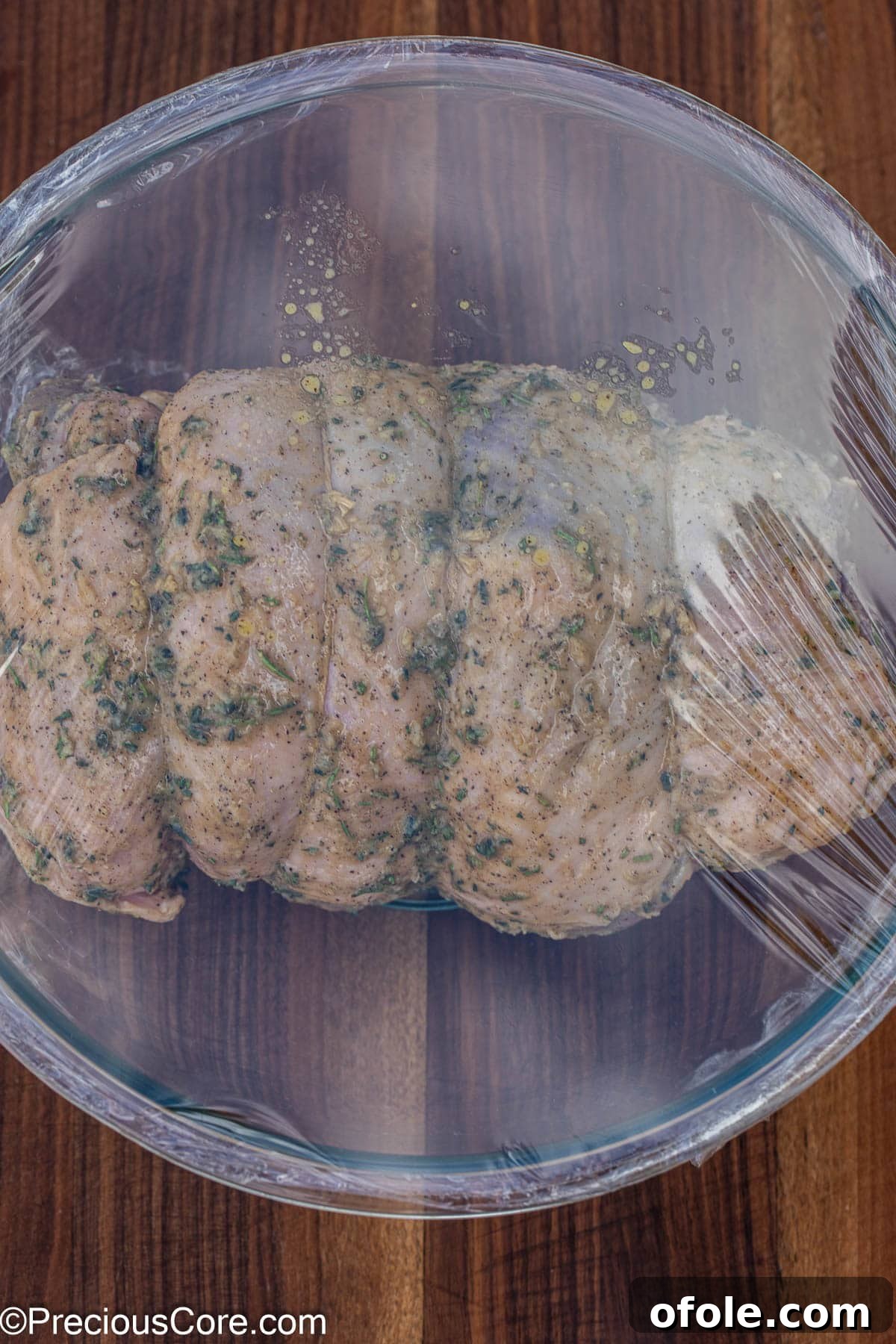 Boneless lamb leg marinating in a mixing bowl, covered with plastic wrap.