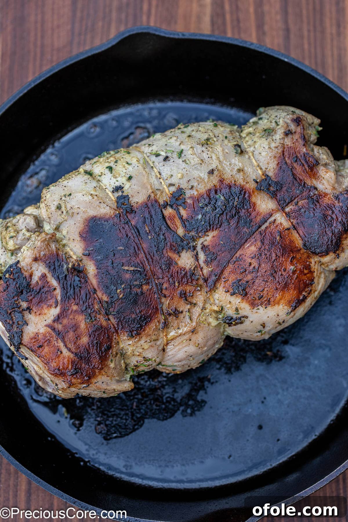 Boneless lamb leg searing in a hot cast iron skillet.