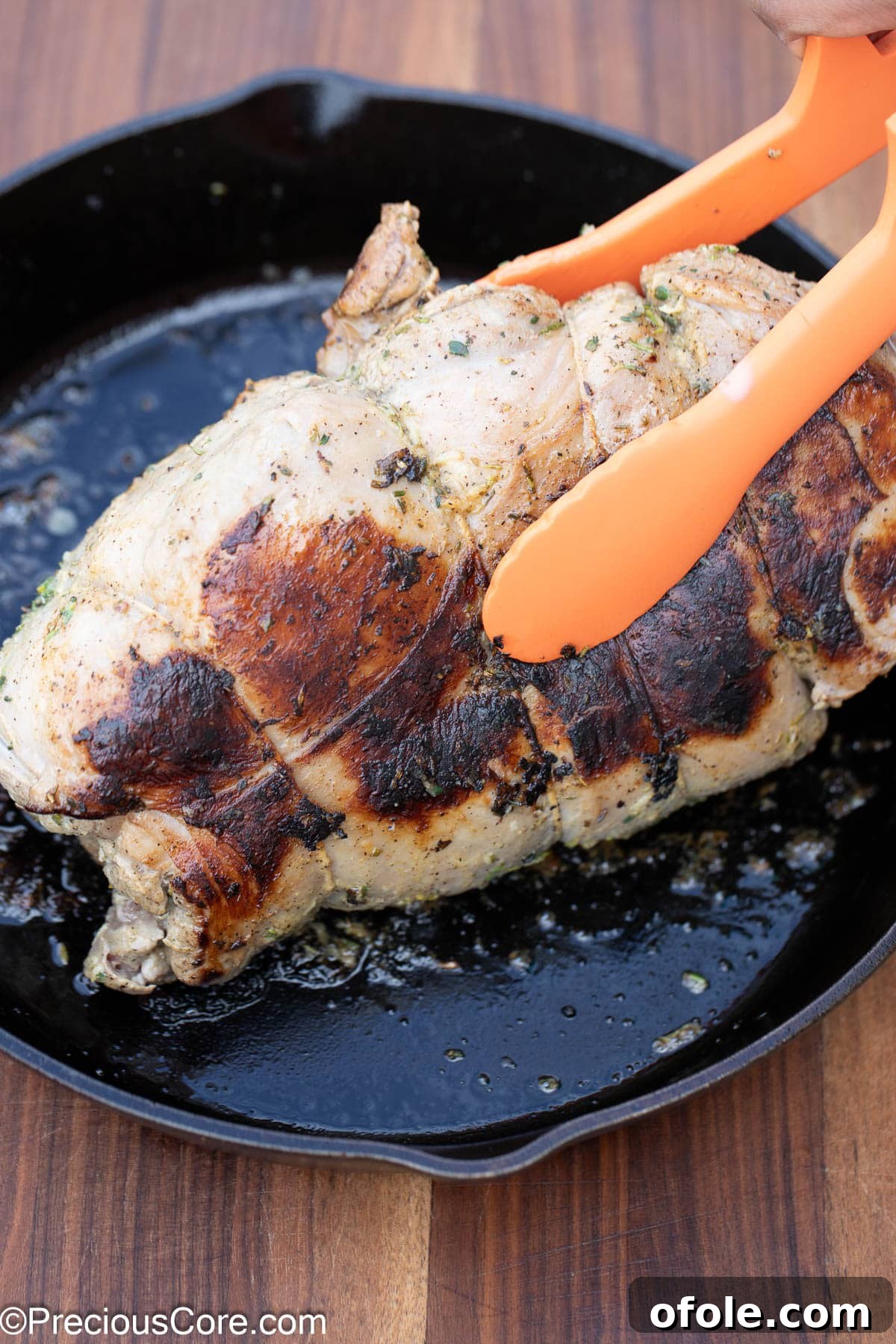 Searing the various sides of a boneless lamb leg to achieve an even crust.