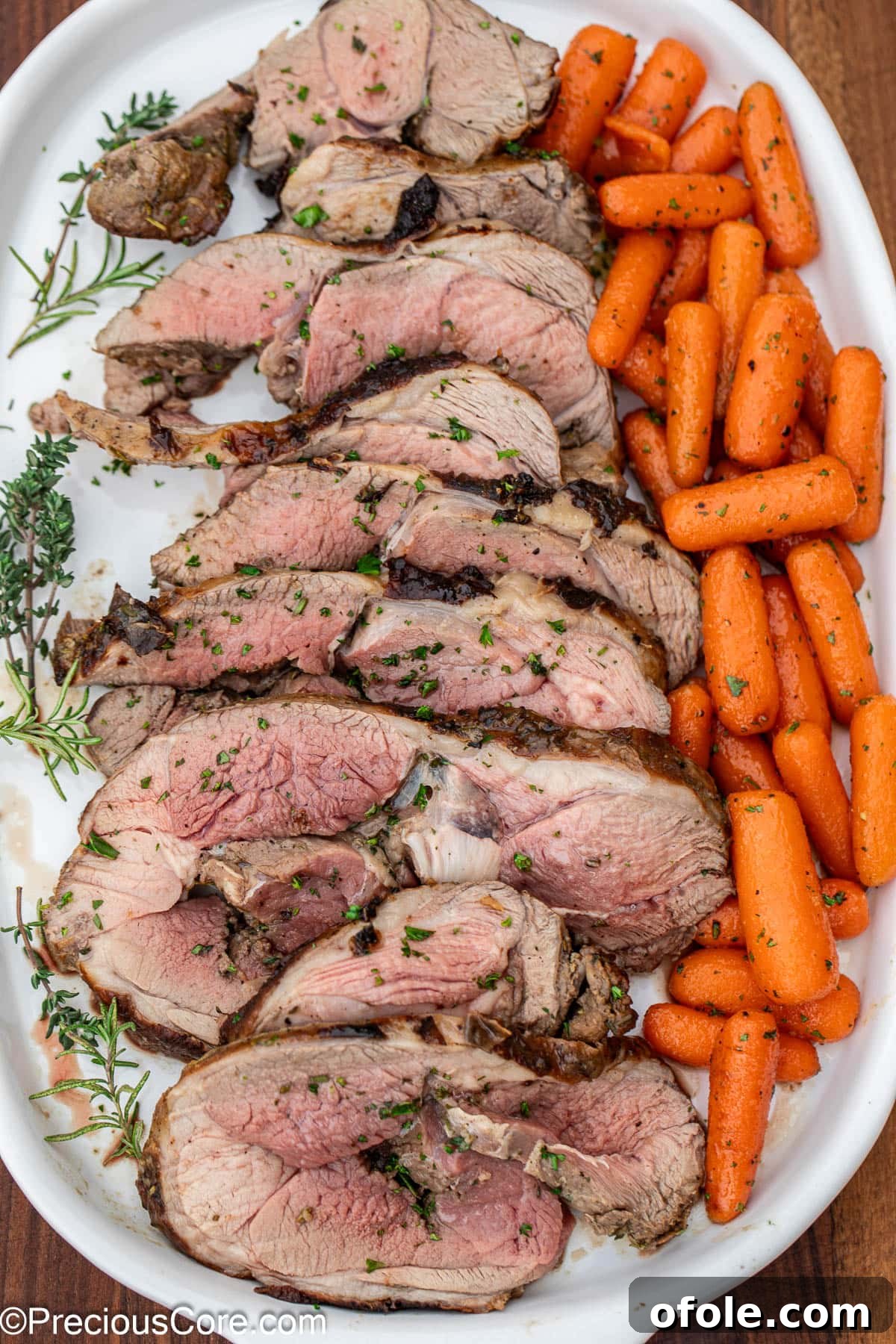 Slices of roasted lamb and glistening glazed carrots arranged neatly on a white serving tray.