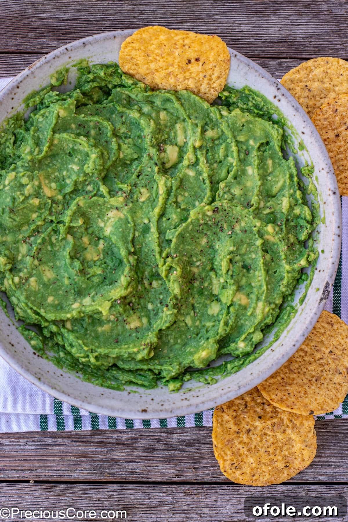 Freshly made guacamole in a vibrant green bowl, with a single golden tortilla chip perfectly poised for dipping.