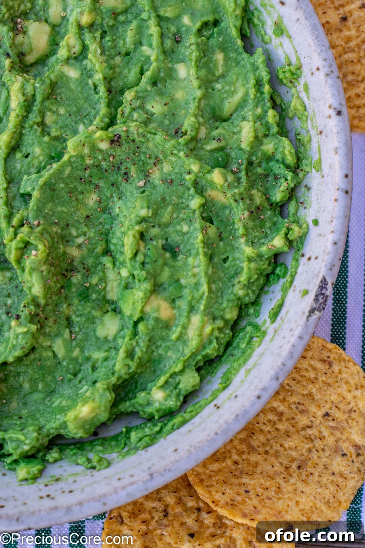 A bowl of vibrant green 4-ingredient guacamole, garnished with a sprinkle of pepper, surrounded by golden, crispy tortilla chips, inviting a dip.