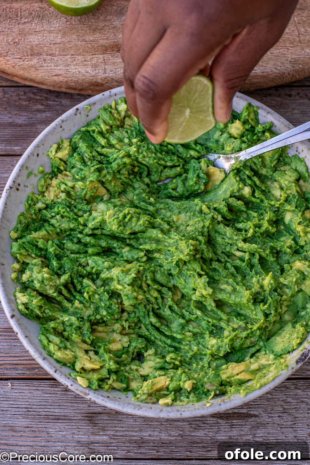 A hand squeezing fresh lime juice directly onto the mashed avocados in a bowl, illustrating the crucial step for flavor and freshness.