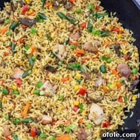 A large wok filled with richly seasoned African Fried Rice, brimming with vegetables and aromatics.