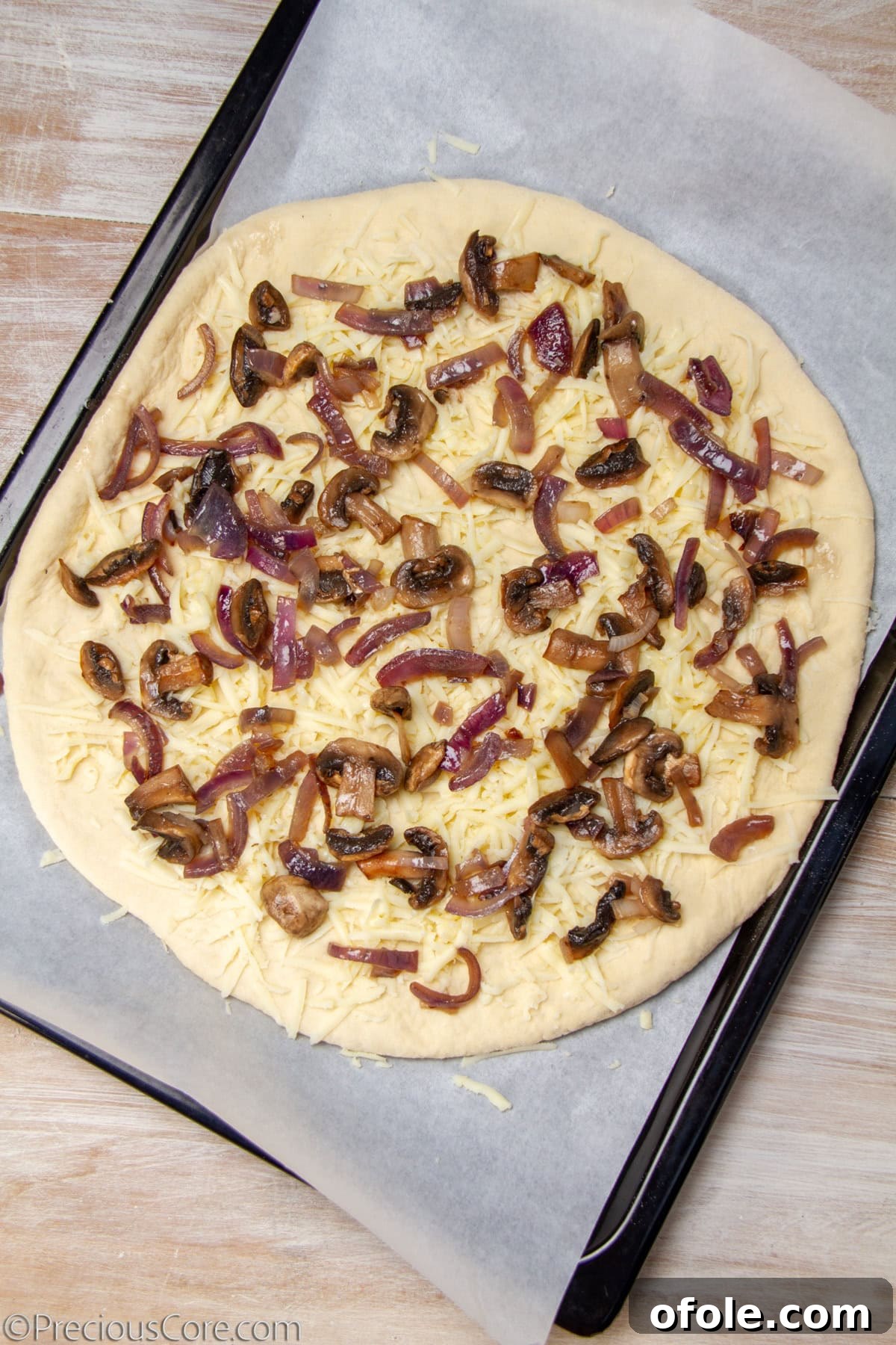 Homemade Mushroom Pizza Perfection 14 An uncooked pizza base generously topped with sautéed mushrooms, caramelized onions, and shredded mozzarella cheese.
