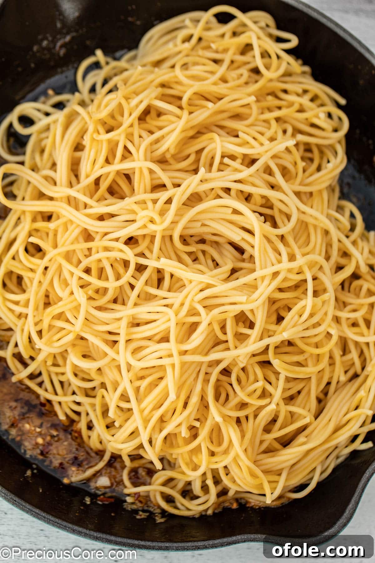 Cooked spaghetti being added to a cast iron pan filled with aromatic garlic butter sauce, ready to be tossed.