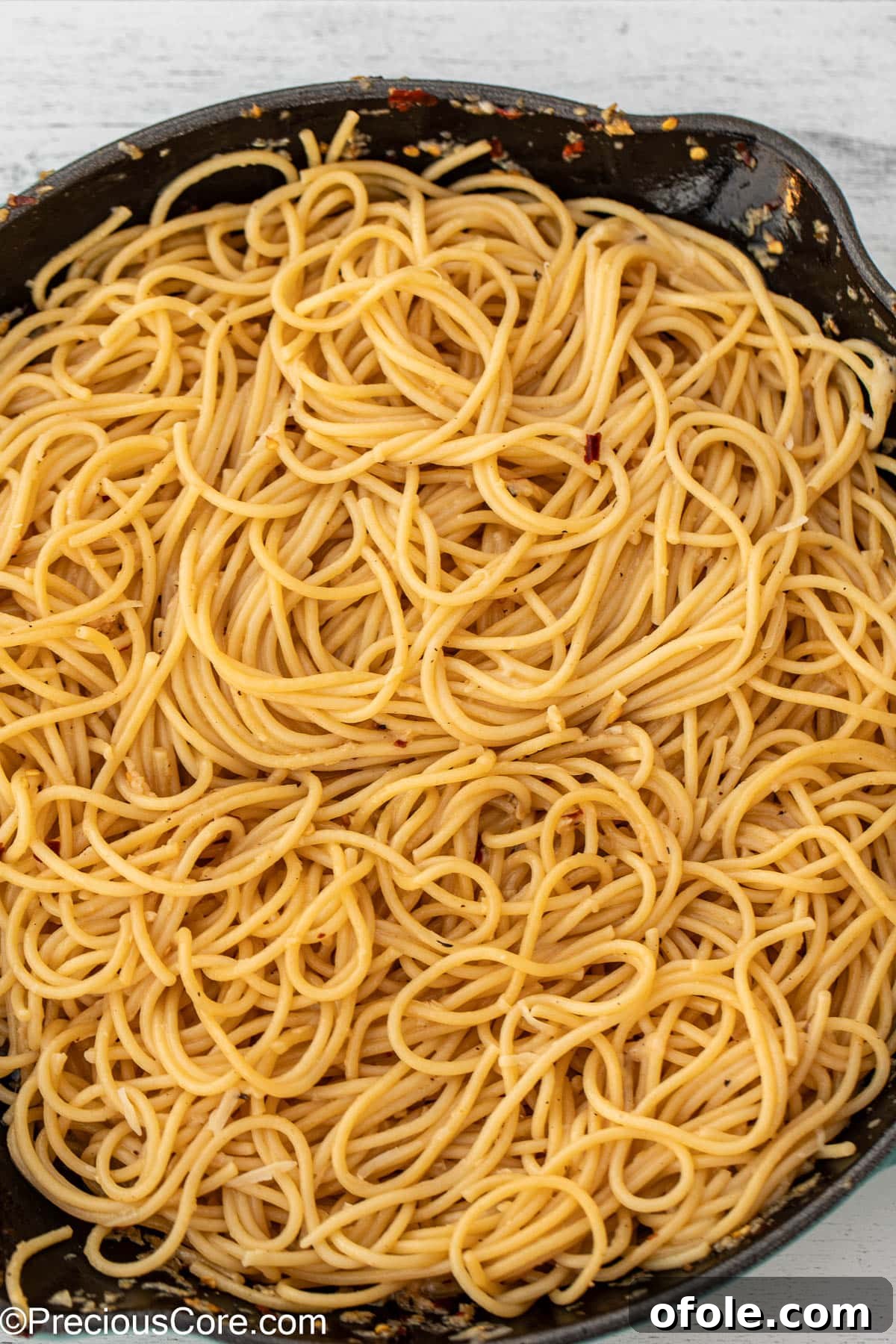 A close-up of spaghetti perfectly tossed and coated in a glistening garlic butter sauce within a pan.
