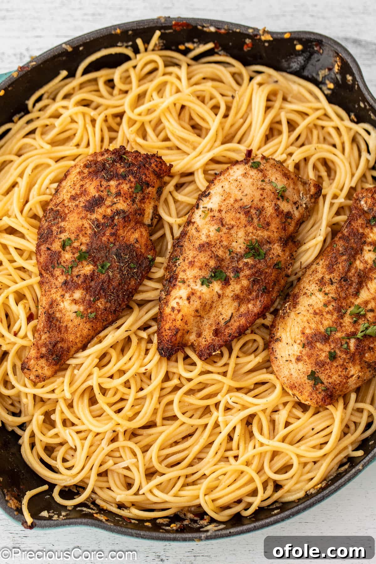 A vibrant skillet filled with golden garlic butter spaghetti, generously topped with tender, seared chicken pieces.