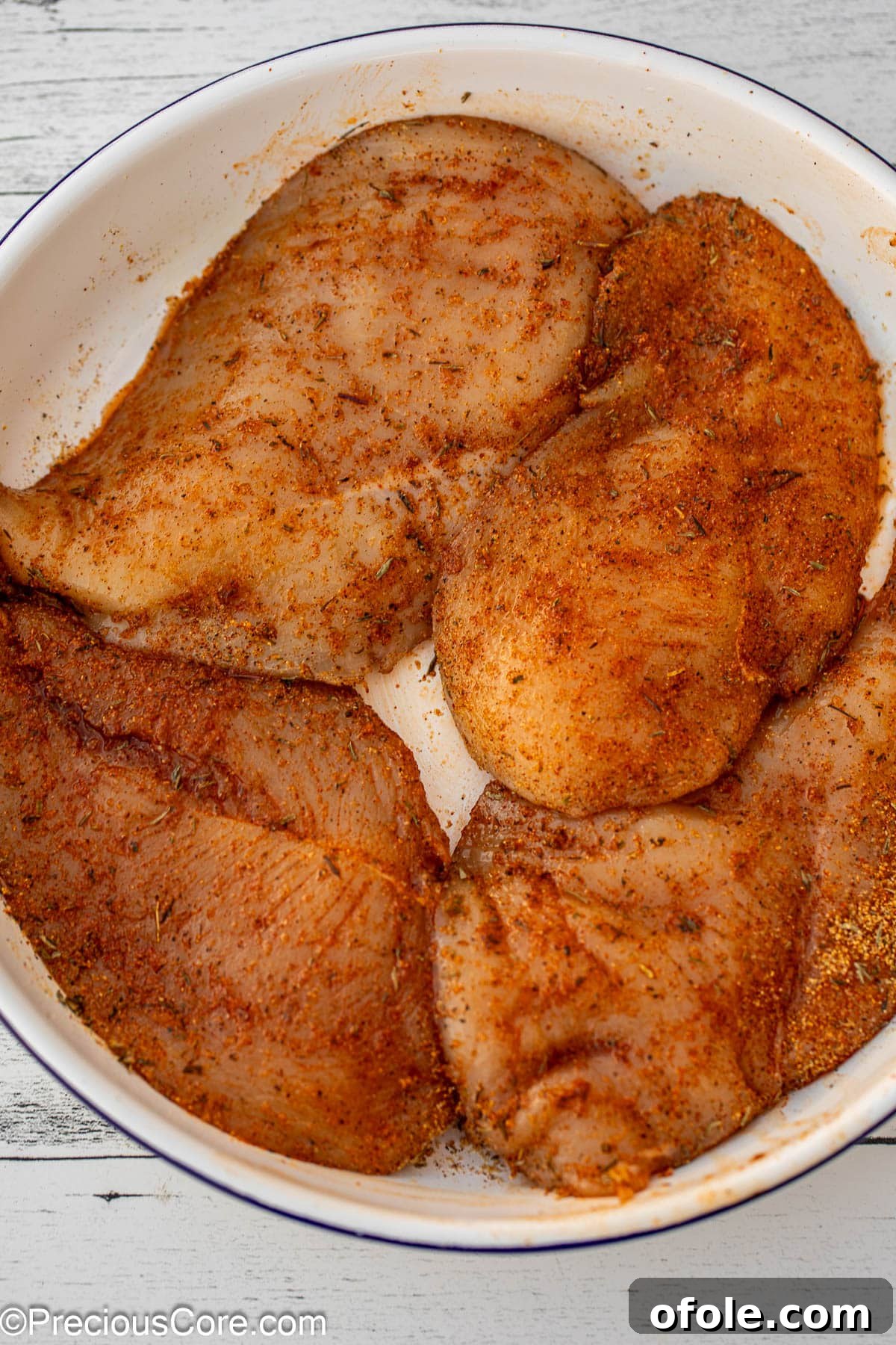 Raw, thinly sliced chicken breasts, perfectly seasoned with various spices, ready for cooking.