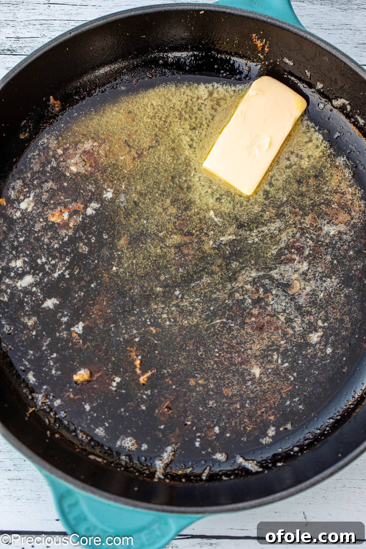 A knob of butter melting and sizzling in a black cast iron skillet over medium heat.