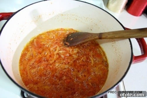 Ultimate Poulet DG Recipe 13 Wooden spoon stirring a pan with tomatoes.