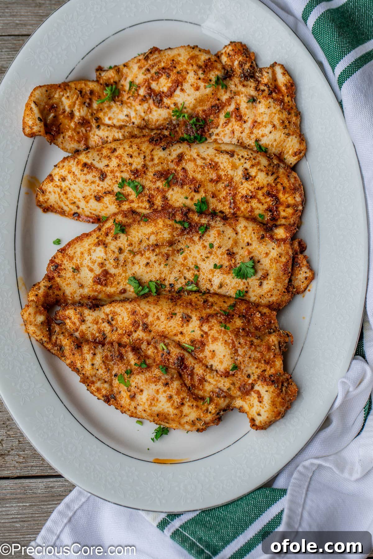 Cooked thin chicken breasts arranged neatly on a white serving plate, garnished for presentation.