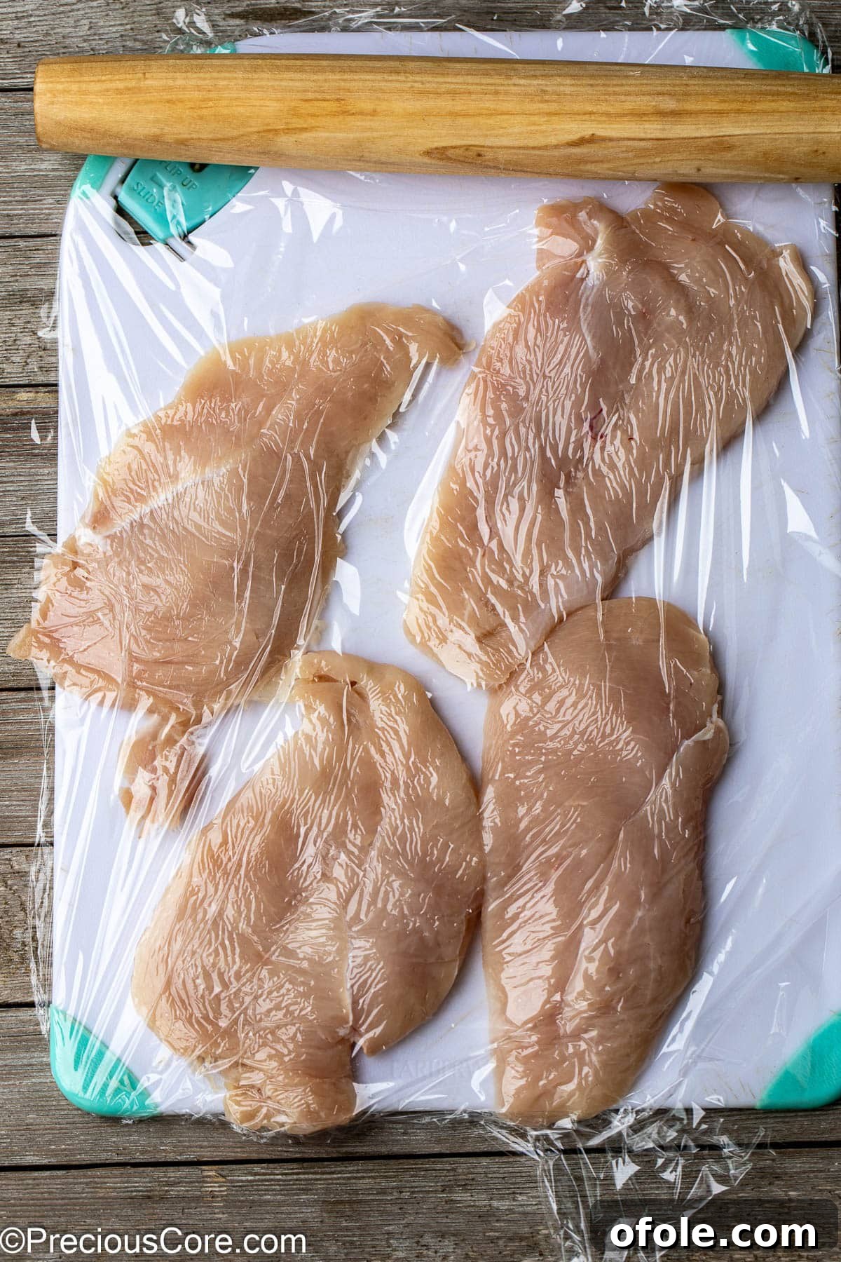 Chicken breasts being flattened with a rolling pin on a cutting board, demonstrating preparation.