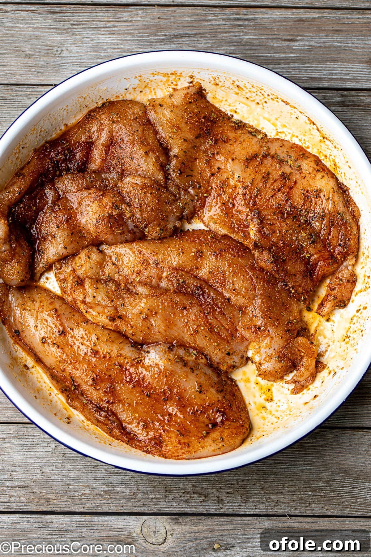Seasoned thin chicken breasts ready for baking in a white mixing bowl.