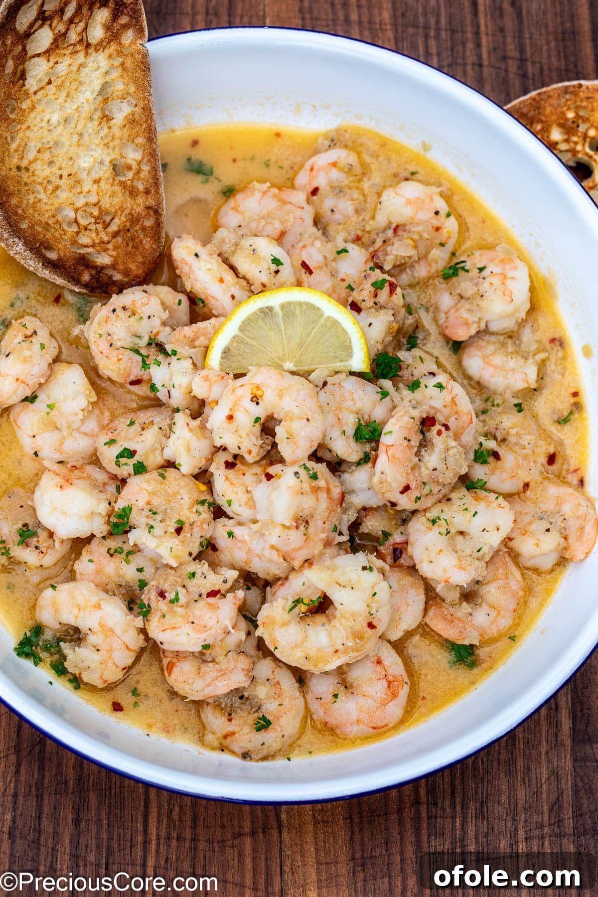 Crusty bread in a bowl of shrimp in white wine sauce.