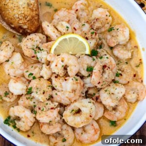 Crusty bread in a bowl of shrimp in white wine sauce.