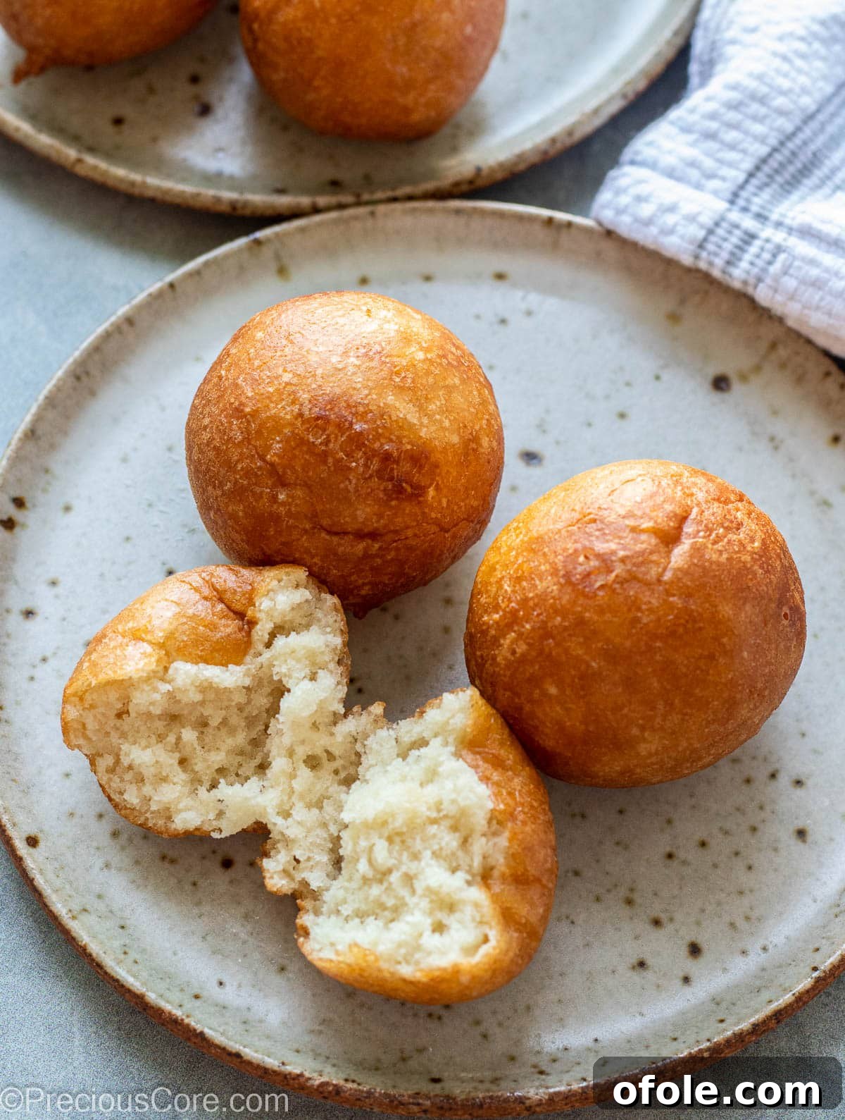 Homemade Fluffy Puff Puff 5 A trio of Puff Puff balls on a plate, one gently pulled apart to show its tender, light texture.