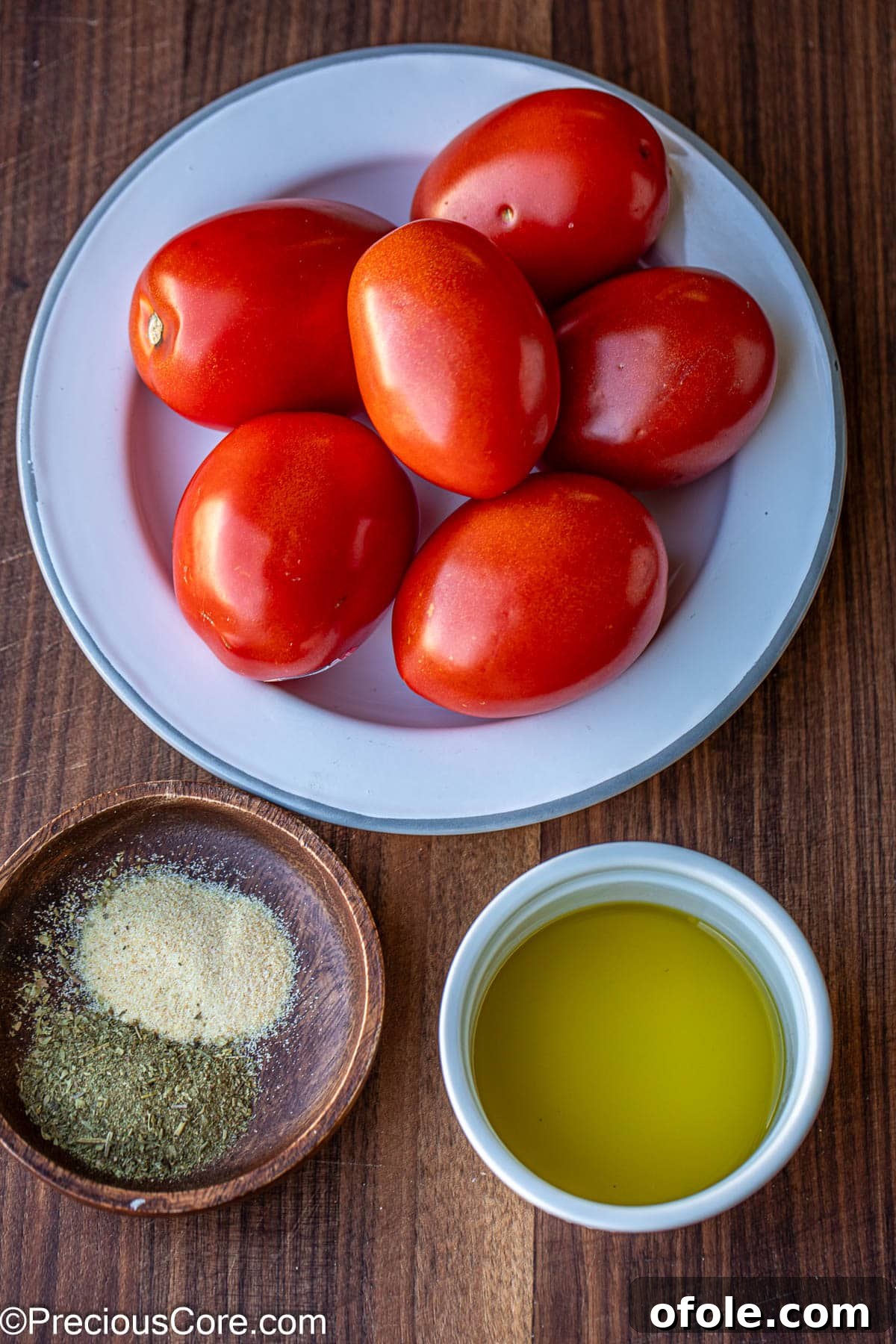 Slow Roasted Tomato Pizza Sauce 3 Fresh Roma tomatoes, a bowl of Italian seasoning, and a small bowl of olive oil on a white surface.