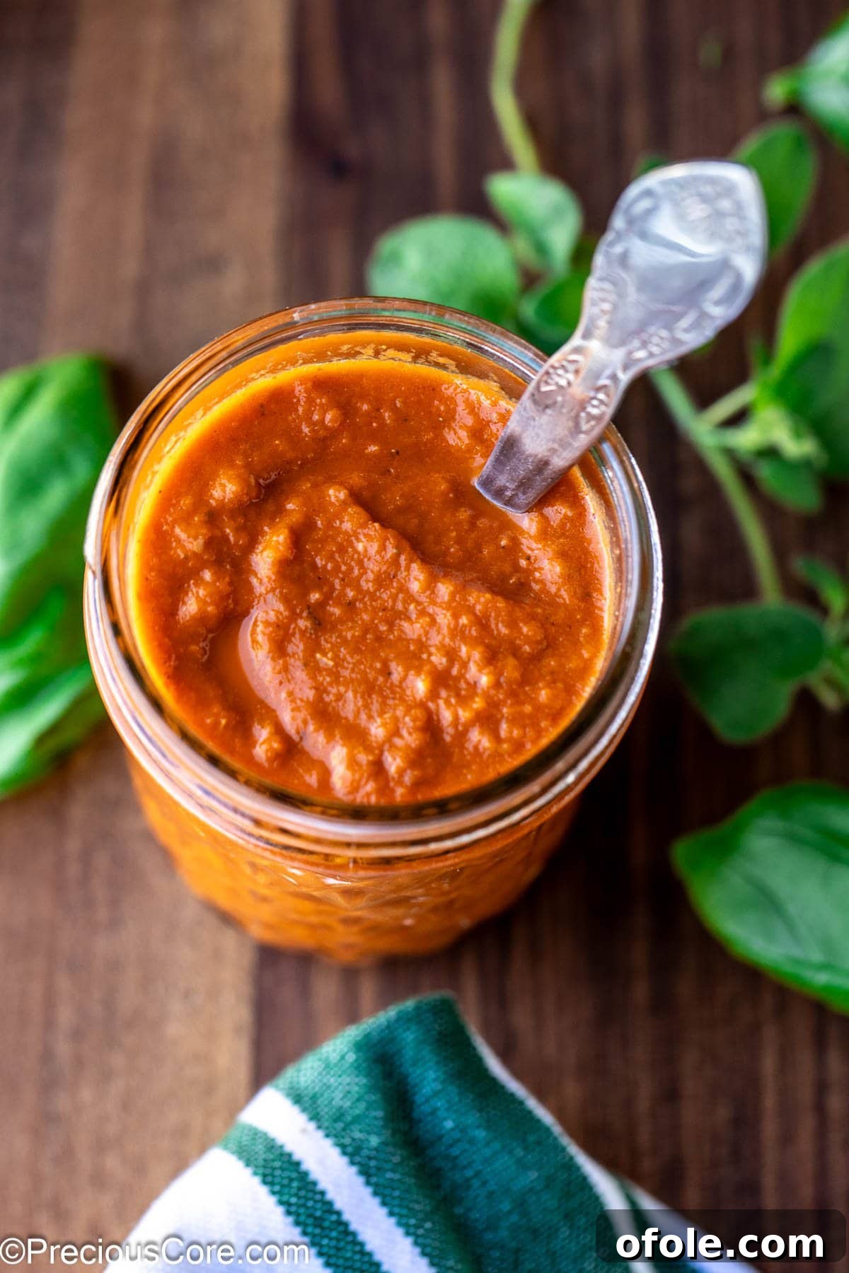 Slow Roasted Tomato Pizza Sauce 9 Homemade roasted tomato pizza sauce stored in a clear mason jar with a label, on a rustic wooden surface.