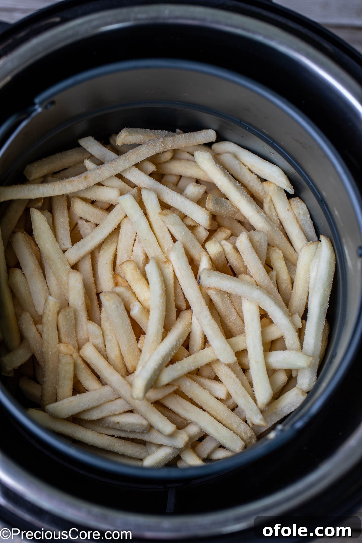 Effortless Crispy Fries in Your Air Fryer 4 Frozen fries spread evenly in a round air fryer basket, ready to cook.
