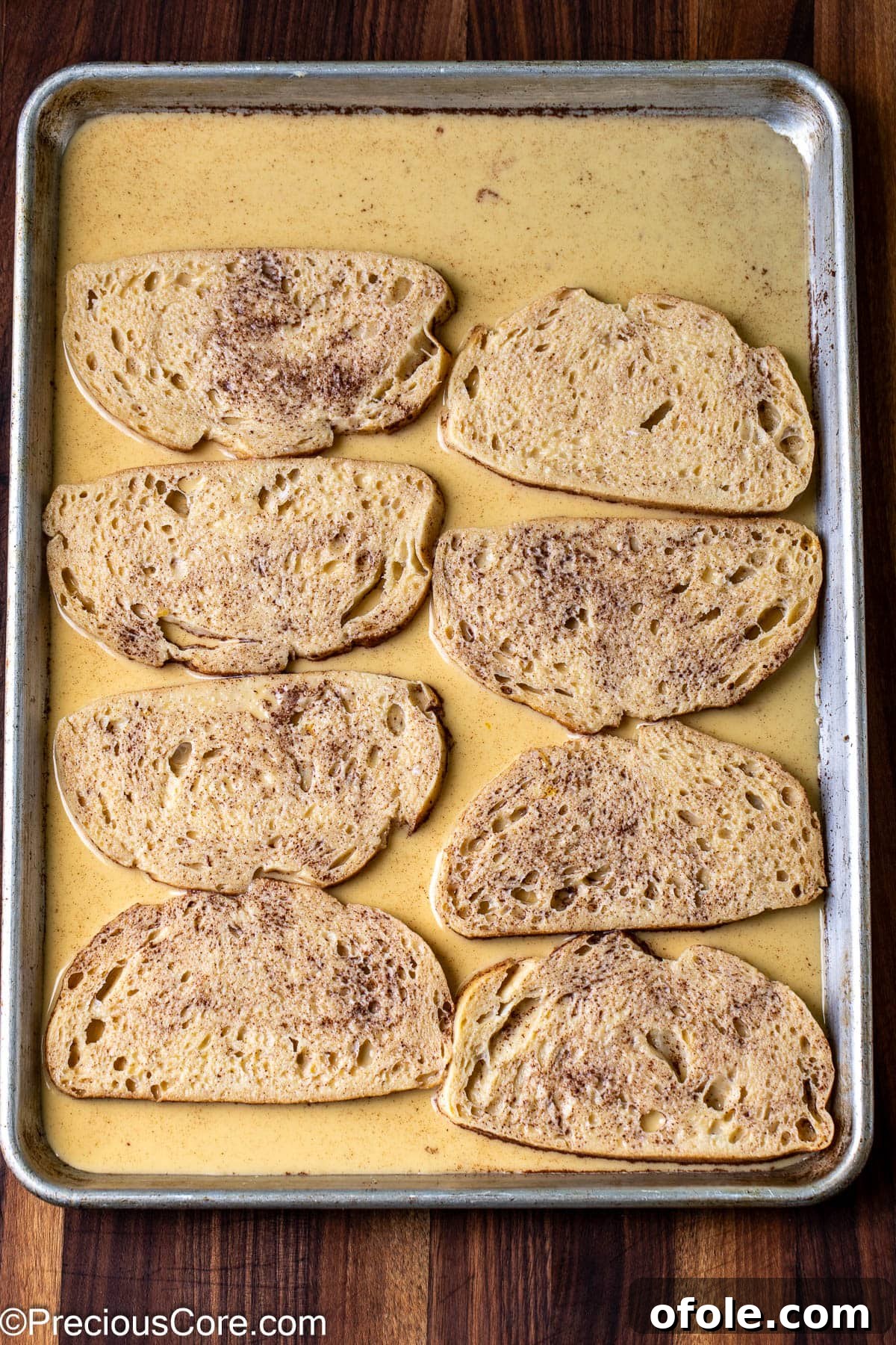 Elevated Sourdough French Toast 7 Slices of sourdough bread diligently soaking in a rich, creamy custard mixture on a flat baking sheet.