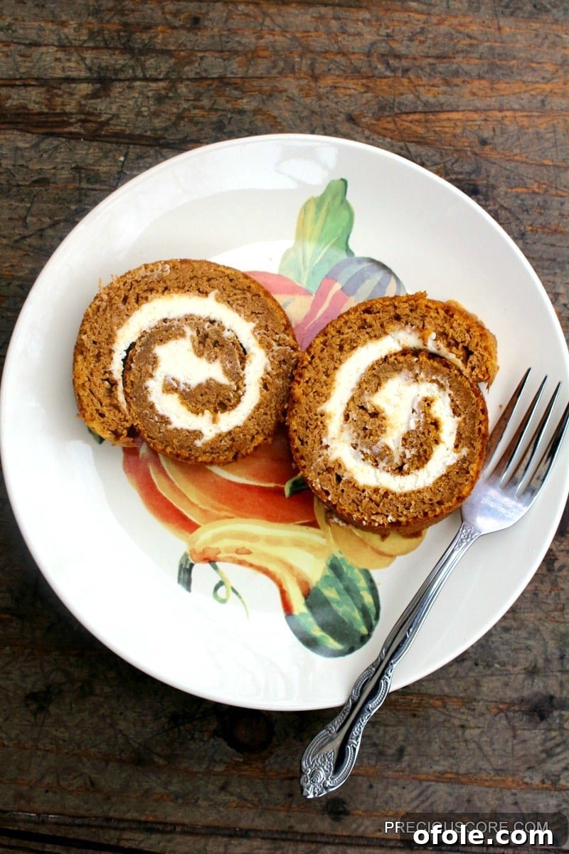 Spiced Pumpkin Swirl Cake 2 Two perfectly sliced pieces of Pumpkin Roll Cake, showcasing the delicate swirl of cake and cream cheese filling, presented on a plate with a fork, ready to be enjoyed.