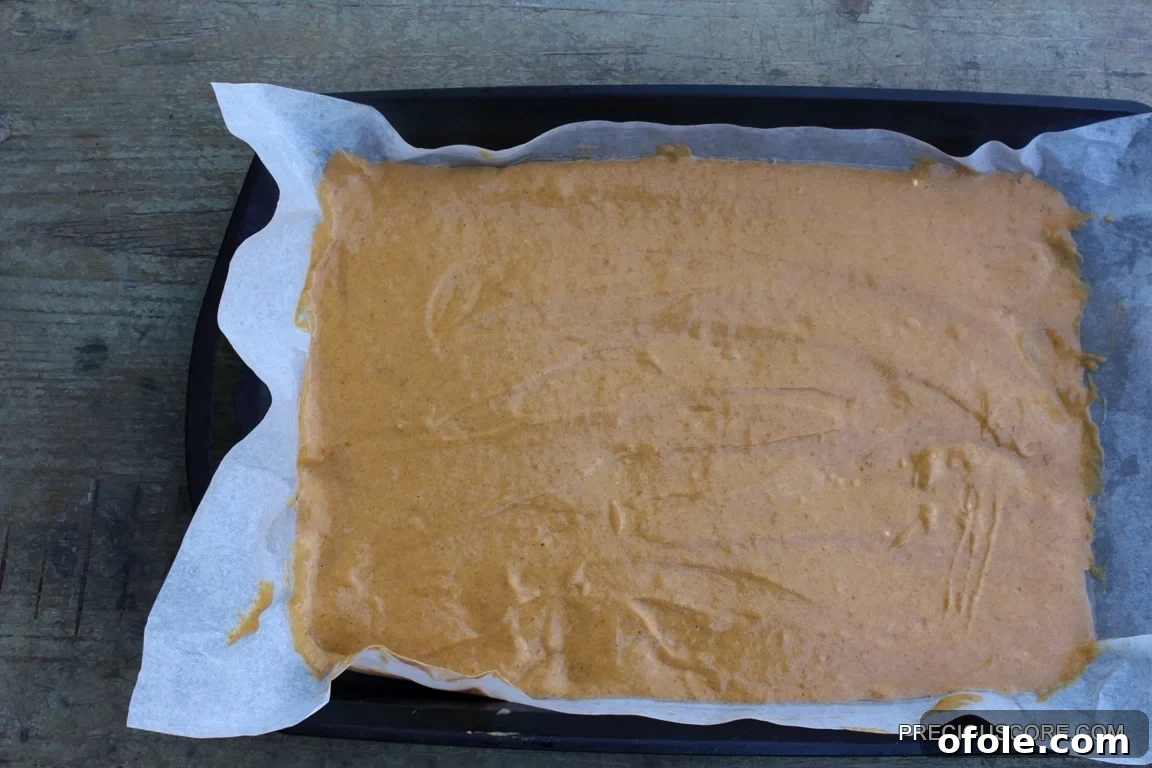 Spiced Pumpkin Swirl Cake 11 Pumpkin roll cake batter meticulously spread into an even layer in a parchment-lined baking pan, prepared for baking.