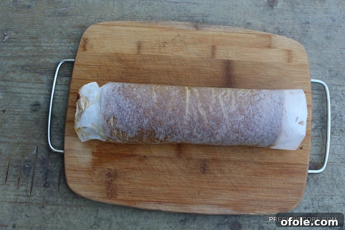 Spiced Pumpkin Swirl Cake 13 A warm pumpkin cake, freshly baked and still wrapped in parchment paper, expertly rolled into a log on a cutting board, ready to cool and set its shape.