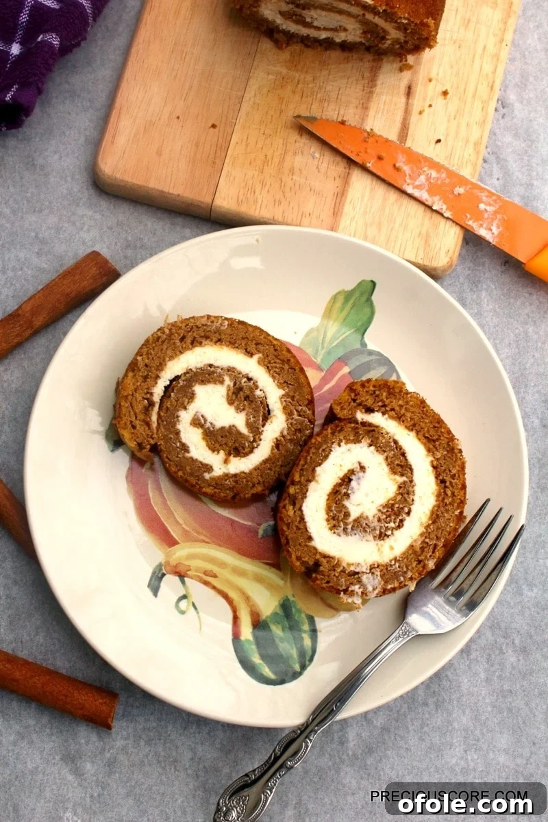 Spiced Pumpkin Swirl Cake 18 Two enticing slices of pumpkin roll cake, garnished with a sprinkle of powdered sugar, presented on a decorative plate with a fork, invitingly ready to be enjoyed as a delightful dessert.