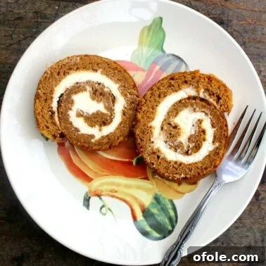 Two slices of pumpkin roll cake on a plate with a fork, ready to be eaten.