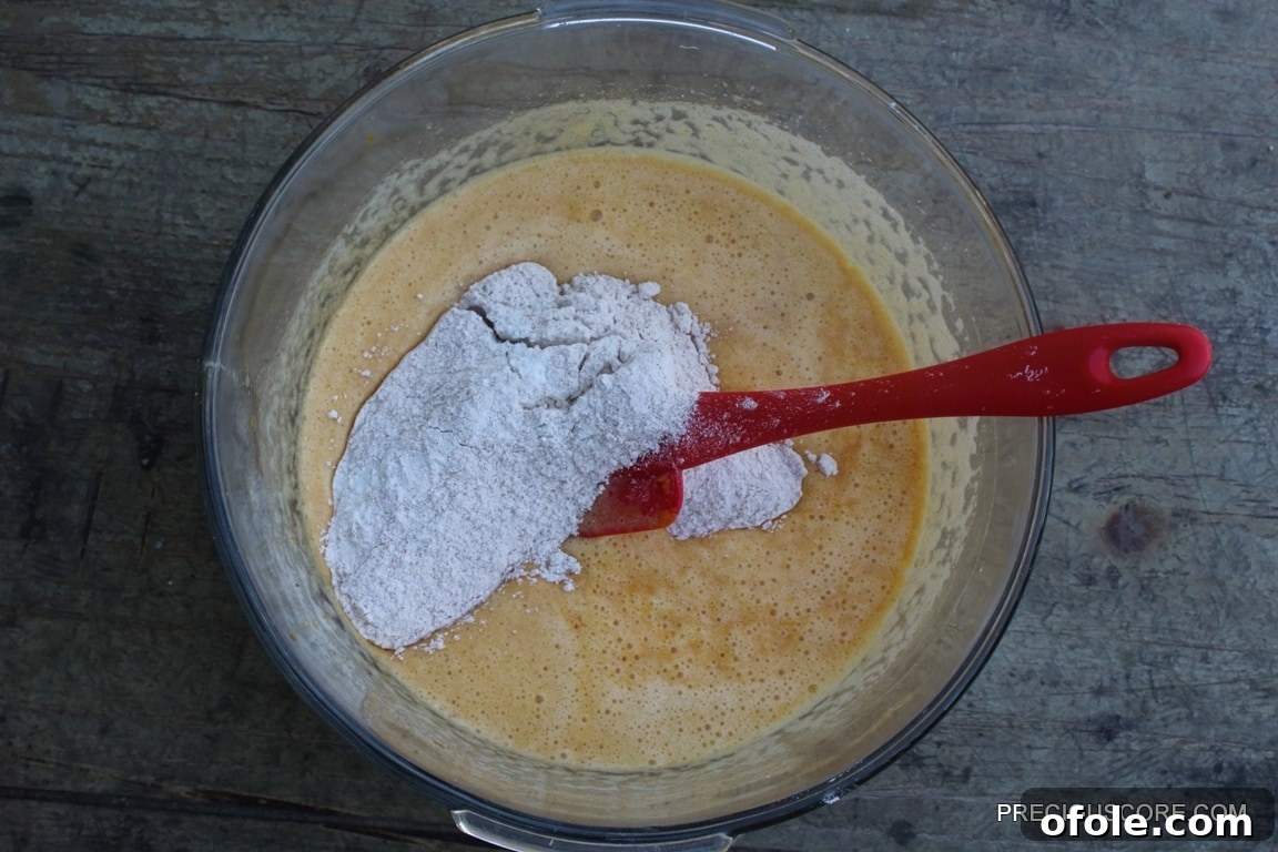Spiced Pumpkin Swirl Cake 9 The wet and dry ingredients for the pumpkin roll cake batter are combined in a mixing bowl, showcasing the rich color and smooth consistency before baking.