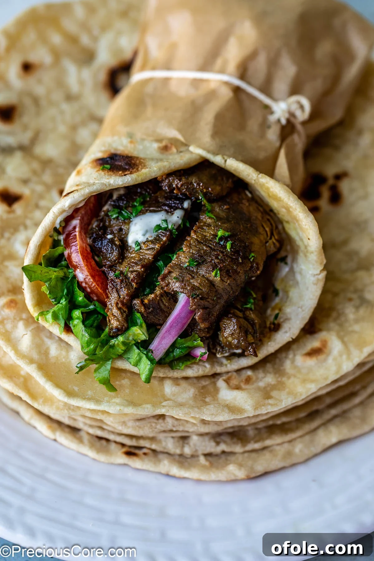 A freshly made beef shawarma wrap, garnished with fresh vegetables and a creamy sauce.