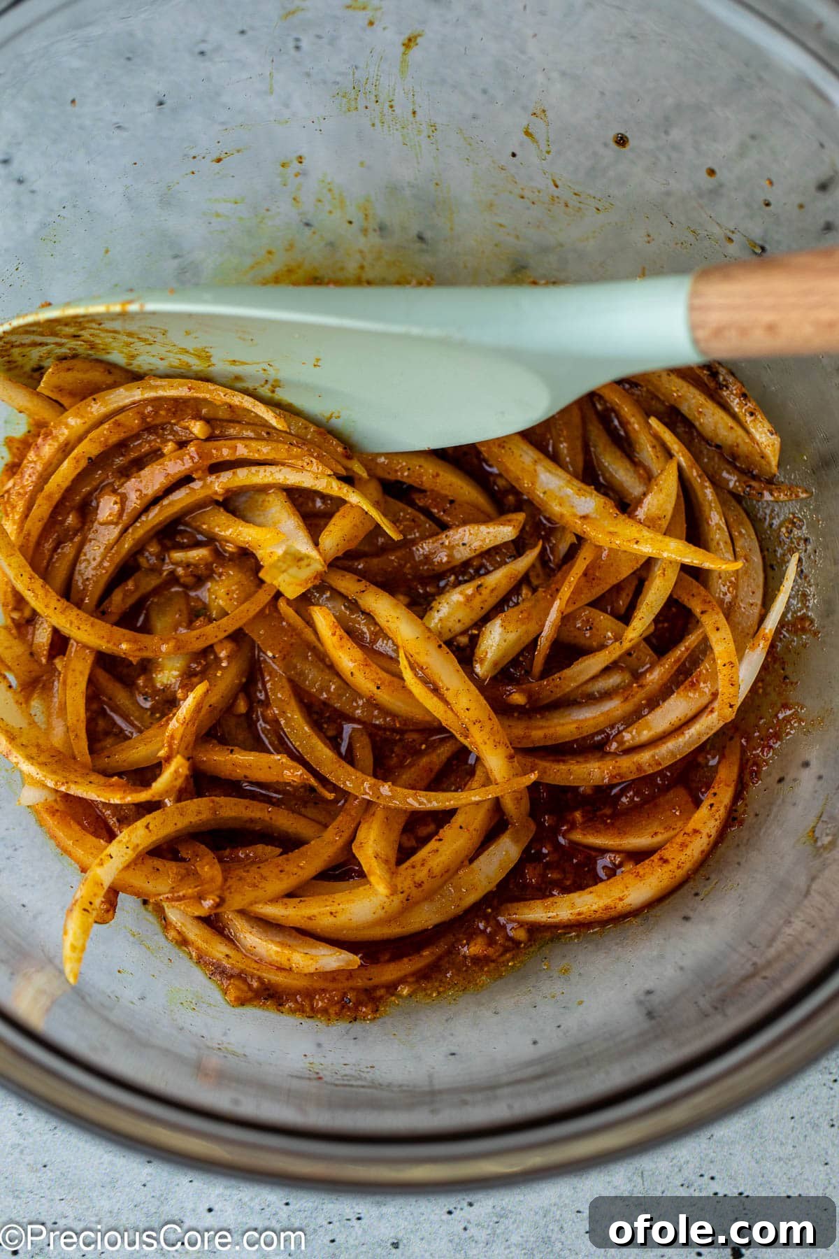 Thinly sliced onions and aromatic marinade ingredients are mixed together in a bowl.