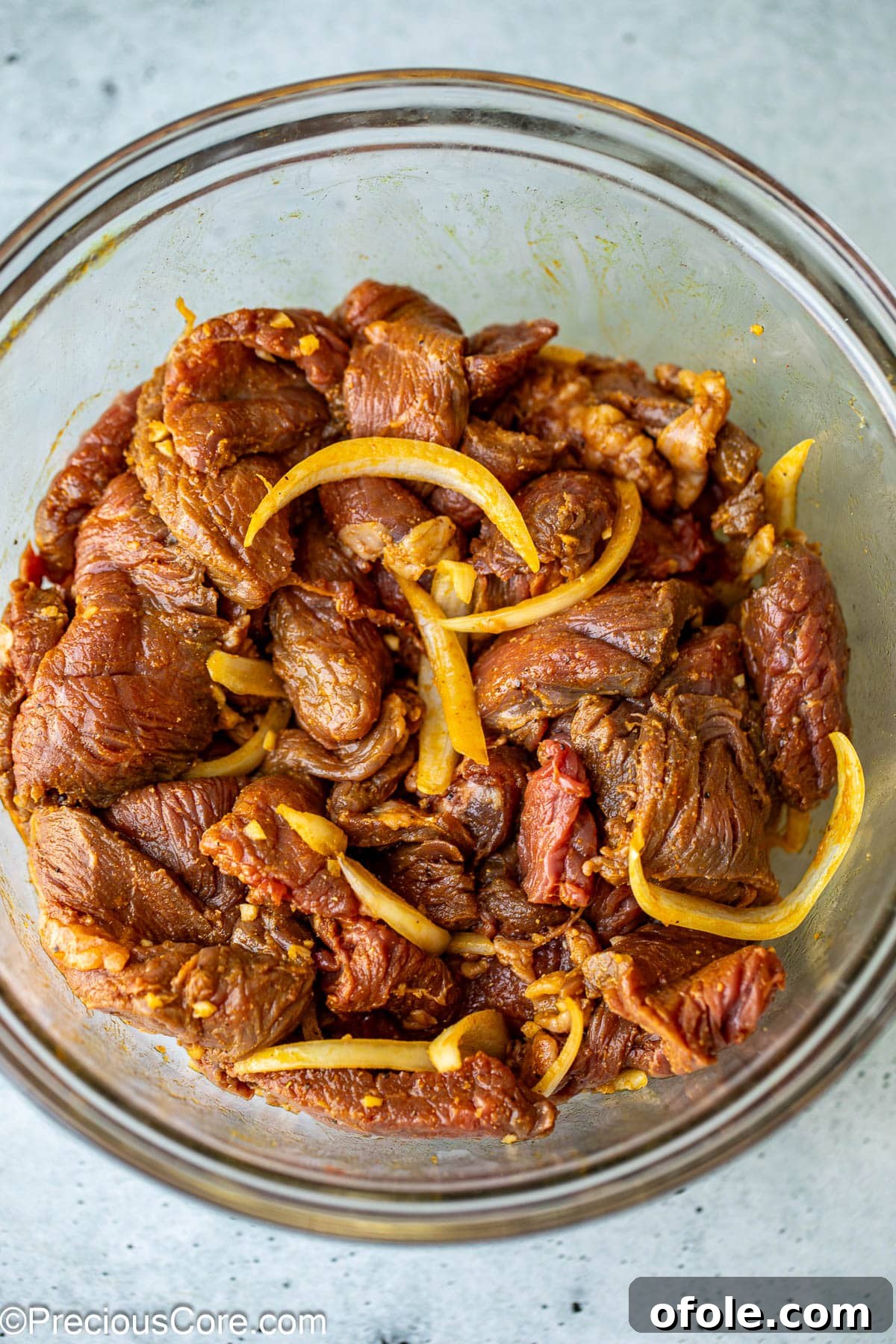 Beef strips being coated in a rich, aromatic marinade in a large mixing bowl.