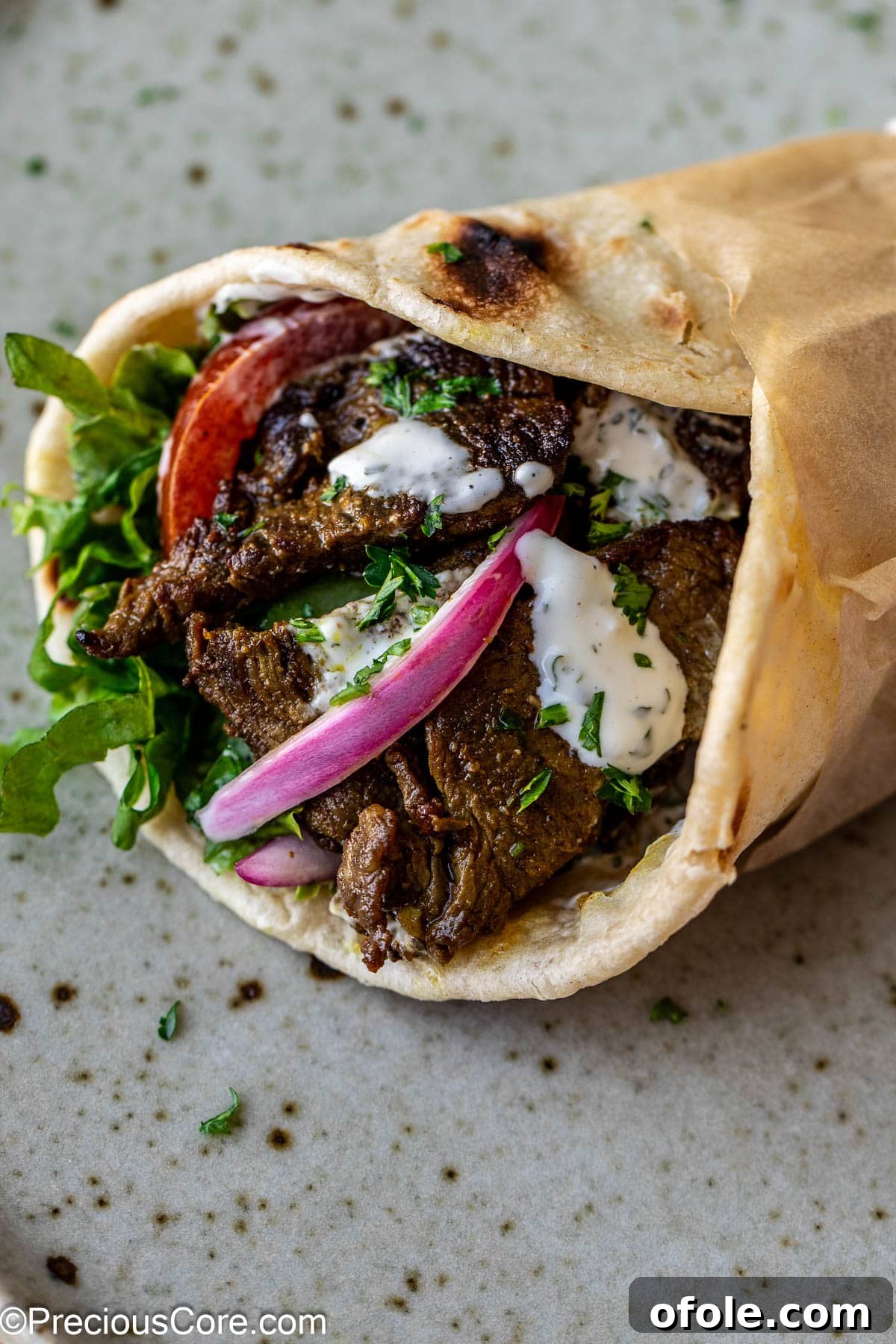 A close-up of a beef shawarma wrap filled with fresh vegetables and drizzled with creamy sauce, inviting a delicious bite.