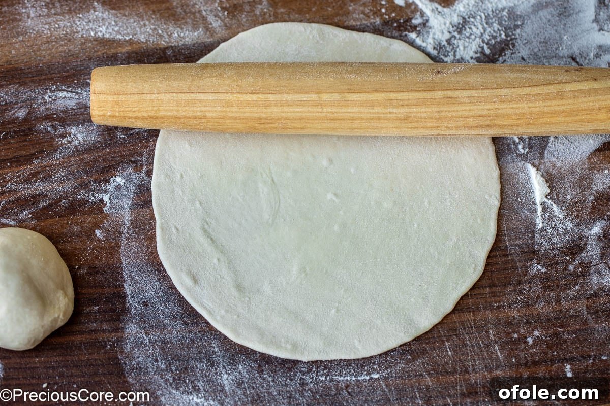 Shawarma Flatbread Delights 9 A rolling pin flattening a piece of dough into a perfect circle on a lightly floured surface.