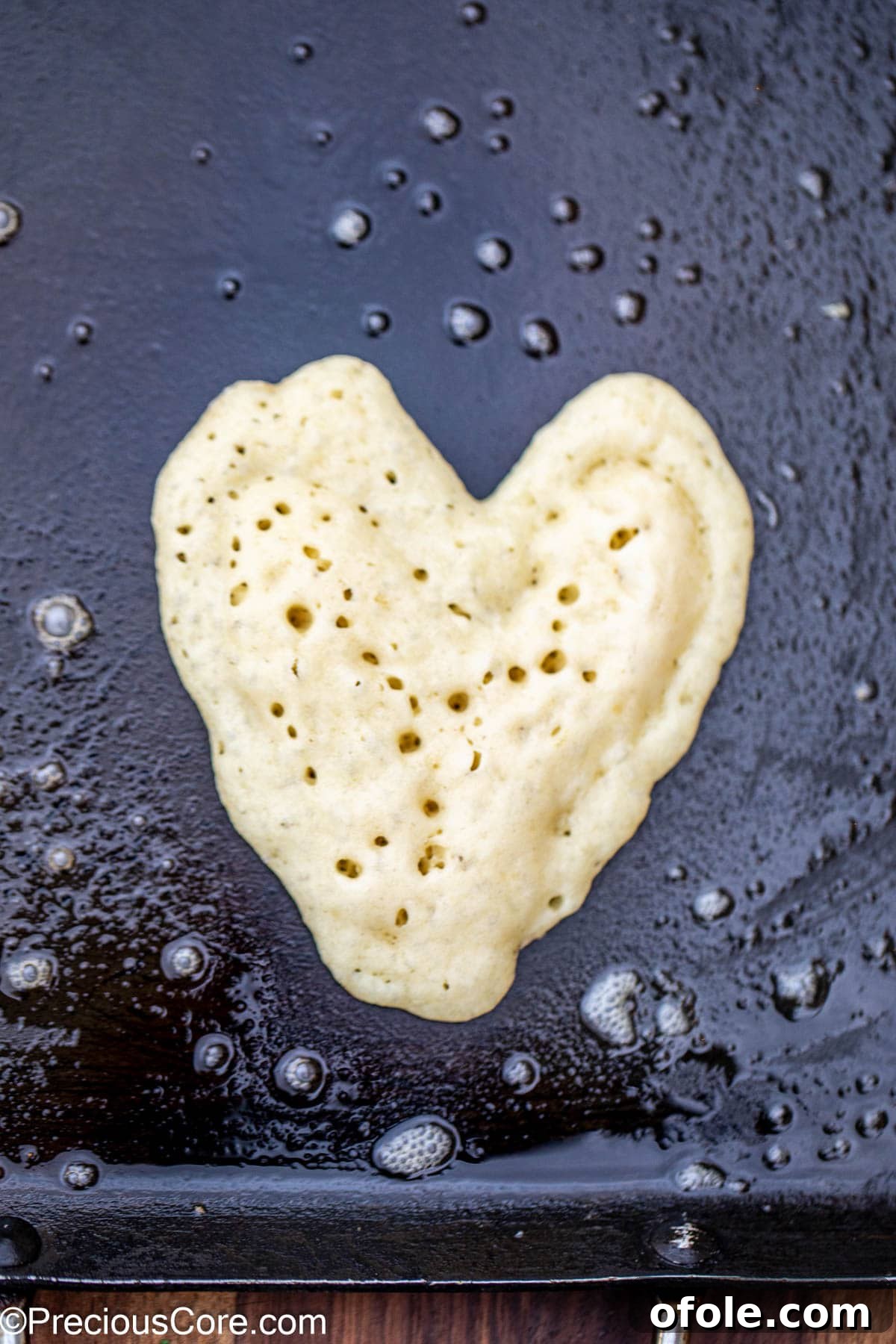 Sweetheart Flapjacks 6 A perfect heart-shaped pancake cooking on a hot griddle, beginning to turn golden brown at the edges.