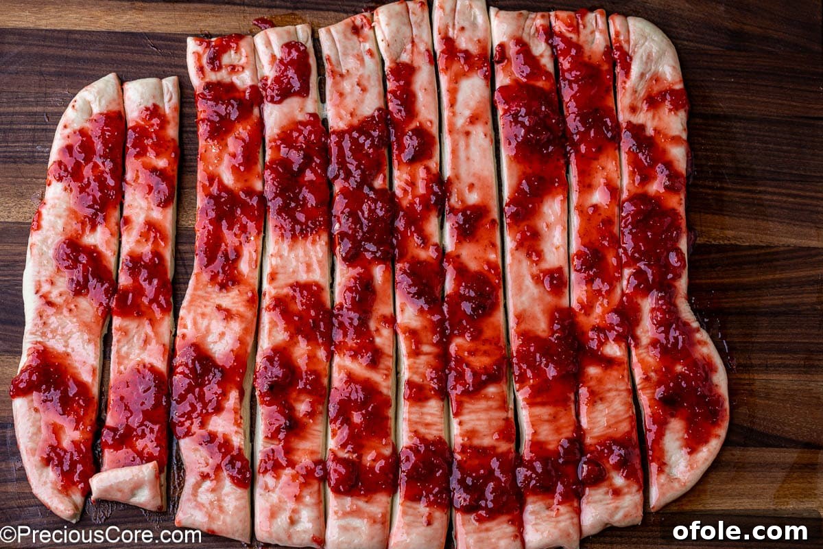 Luscious Strawberry Cinnamon Rolls 14 Cinnamon roll dough cut into uniform strips with strawberry filling visible.