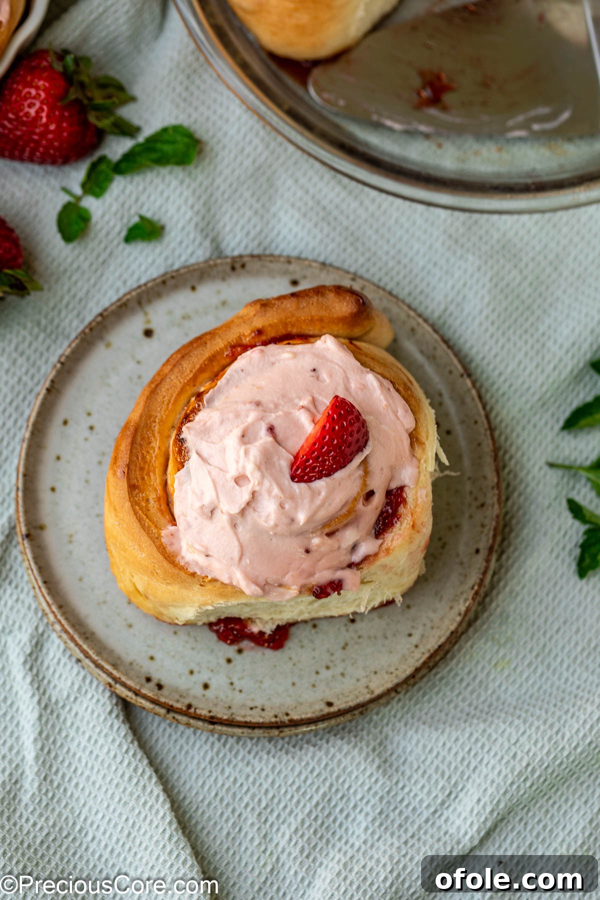 Luscious Strawberry Cinnamon Rolls 20 A single strawberry cinnamon roll on a white dessert plate, beautifully frosted.