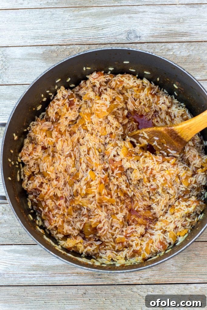 Washed jasmine rice mixed with the flavorful palm oil sauce in a large cooking pot, ready for liquid.