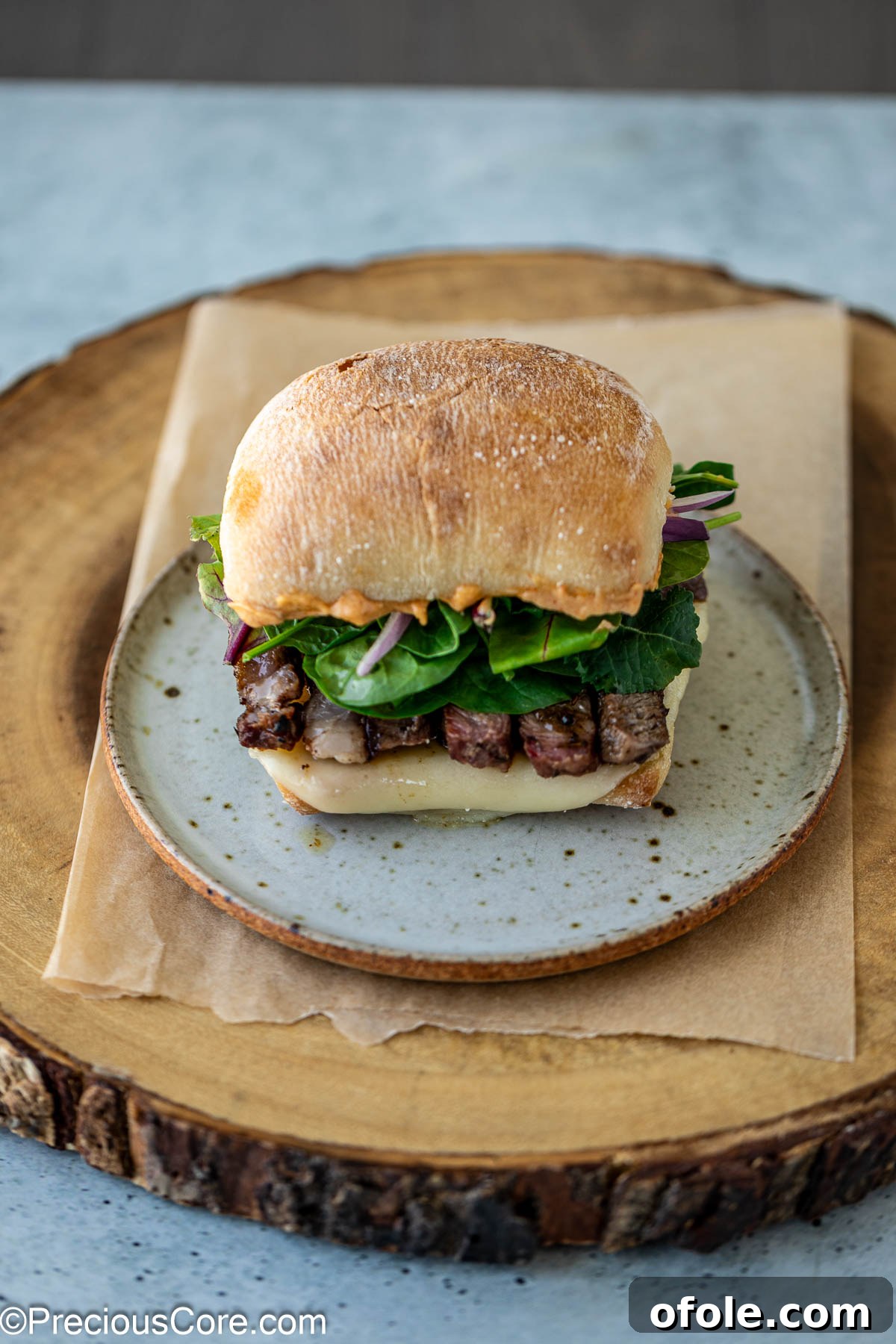 Elevated Ribeye Steak Sandwich 11 Assembled sandwich with ribeye steak, greens, onions, and cheese.