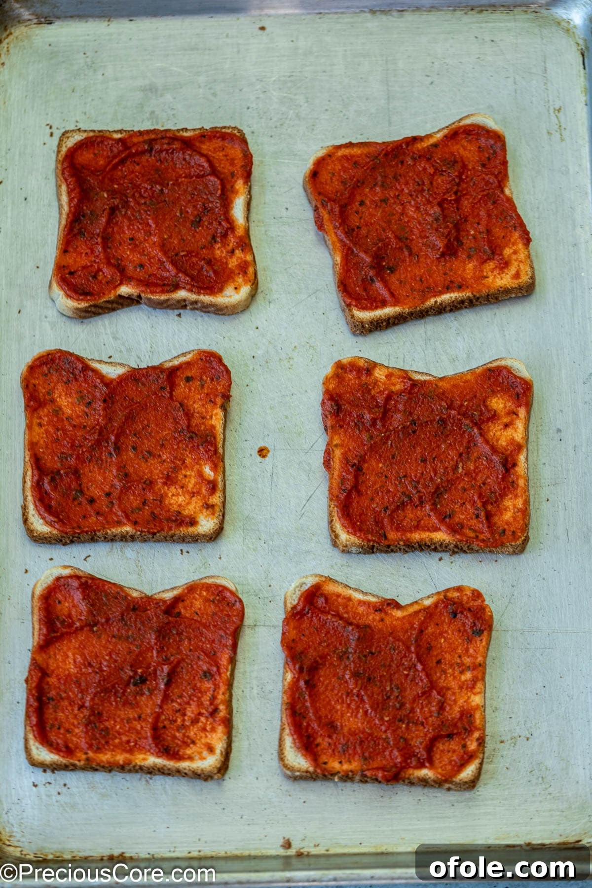 Pizza sauce spread on bread slices.